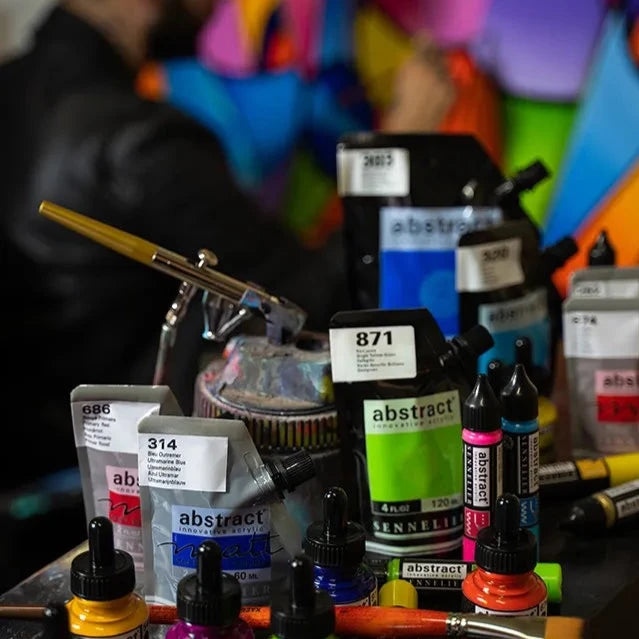 Colourful Art Materials on a table with Artist painting large mural in the background